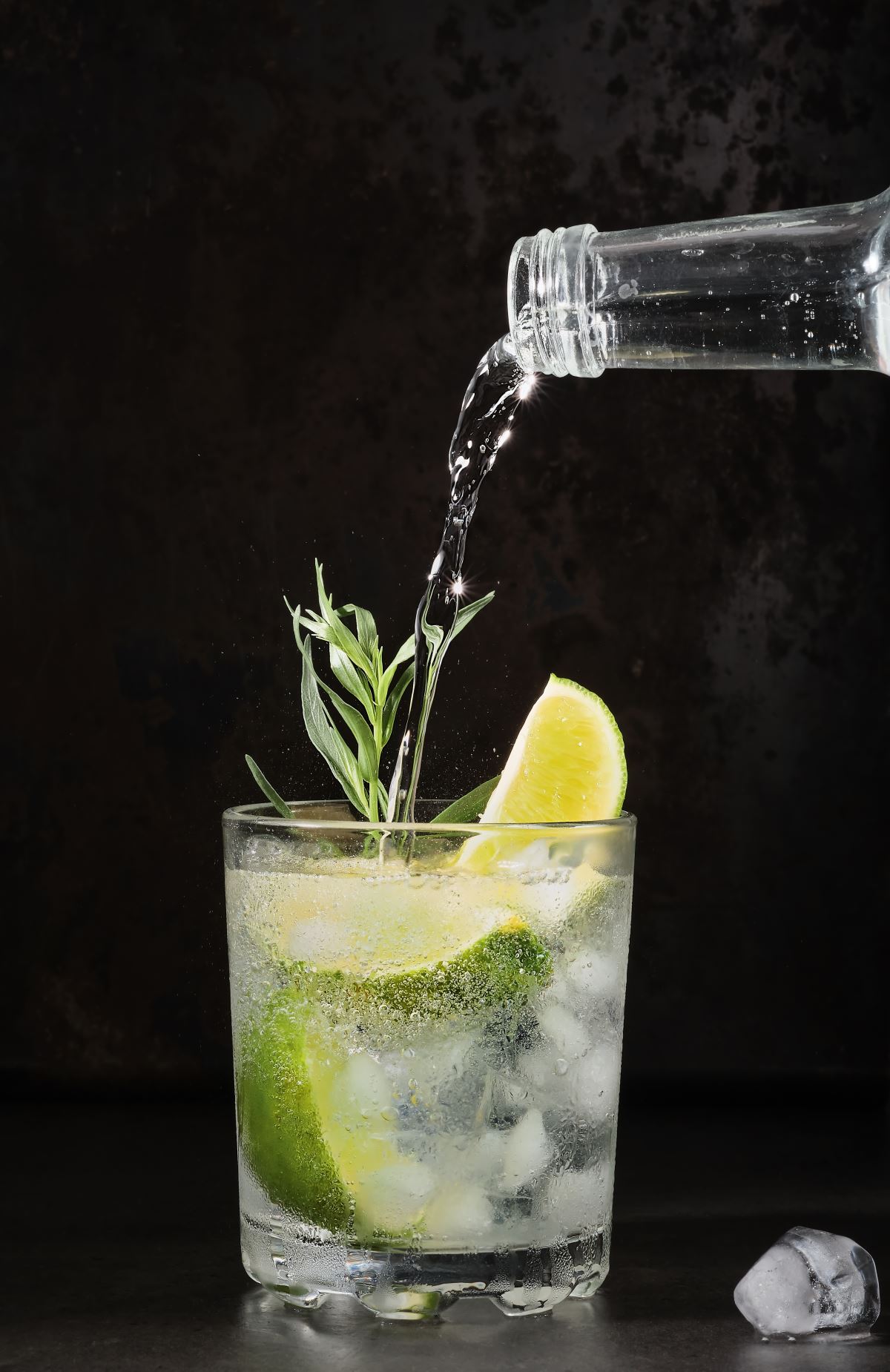 171252393 glass lime lemonade dark table summer drinks pure mineral water is poured into glass vertical frame selective focus homemade drink with lime tarragon ice cubes cold fresh drinks idea